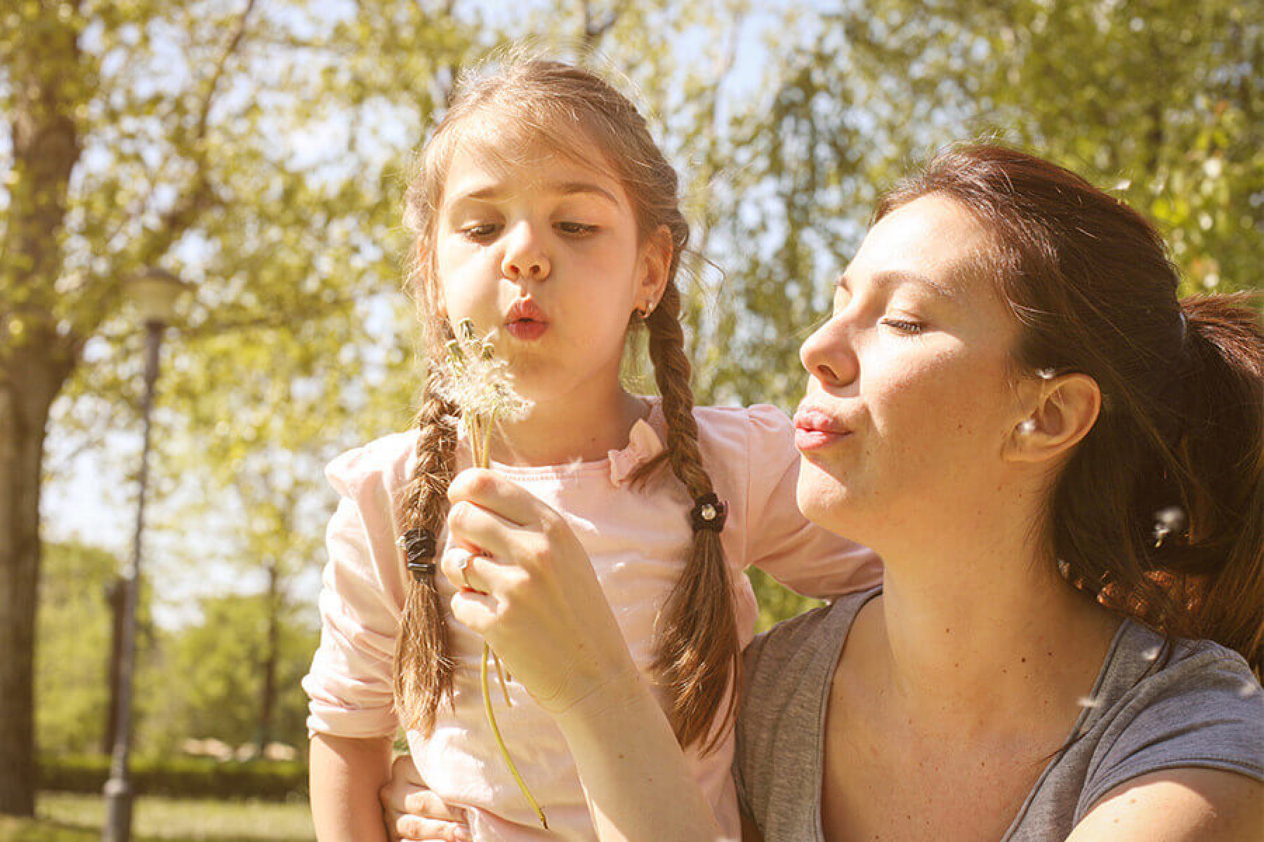 Mutter und Kind beim Ausblasen einer Pusteblume.