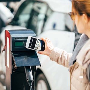 Frau nutzt ihr Handy an einer E-Ladesäule zum Bezahlen.