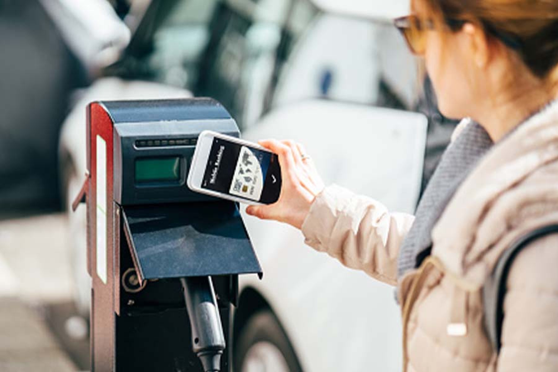 Frau nutzt ihr Handy an einer E-Ladesäule zum Bezahlen.