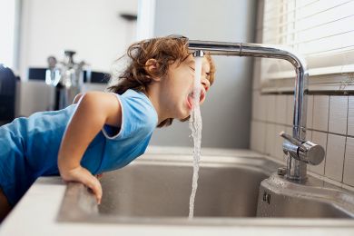 Ein junge trinkt Wasser direkt aus dem Wasserhahn.