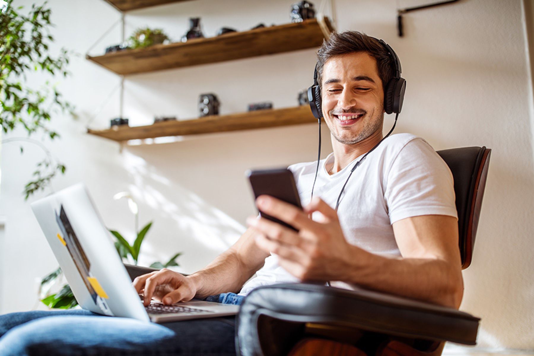 Ein junger Mann nutzt zu Hause sein Laptop und sein Mobiltelefon. 