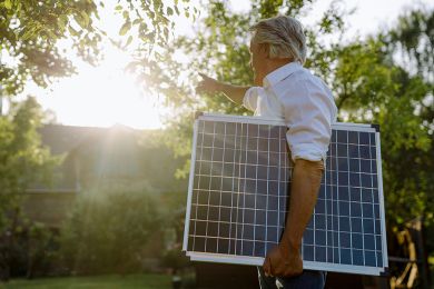 Ein Mann trägt eine Mini-Solaranlage zu seinem Haus.