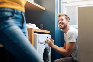 Ein junger Mann stellt in seinem Badezimmer die Waschmaschine an. 