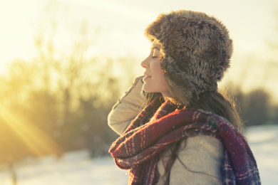 Eine Frau trägt eine warme Fellmütze und hält ihr Gesicht in die Wintersonne.