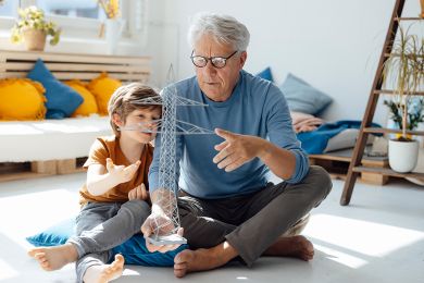 Enkel und Großvater untersuchen das Modell eines Strommastes im Wohnzimmer.