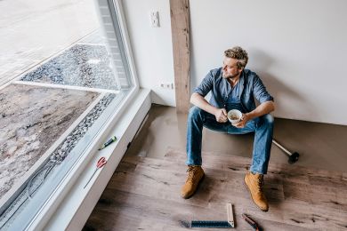 Ein Handwerker sitzt auf dem Fußboden in einem renovierten Haus, macht eine Pause und trinkt Kaffee.