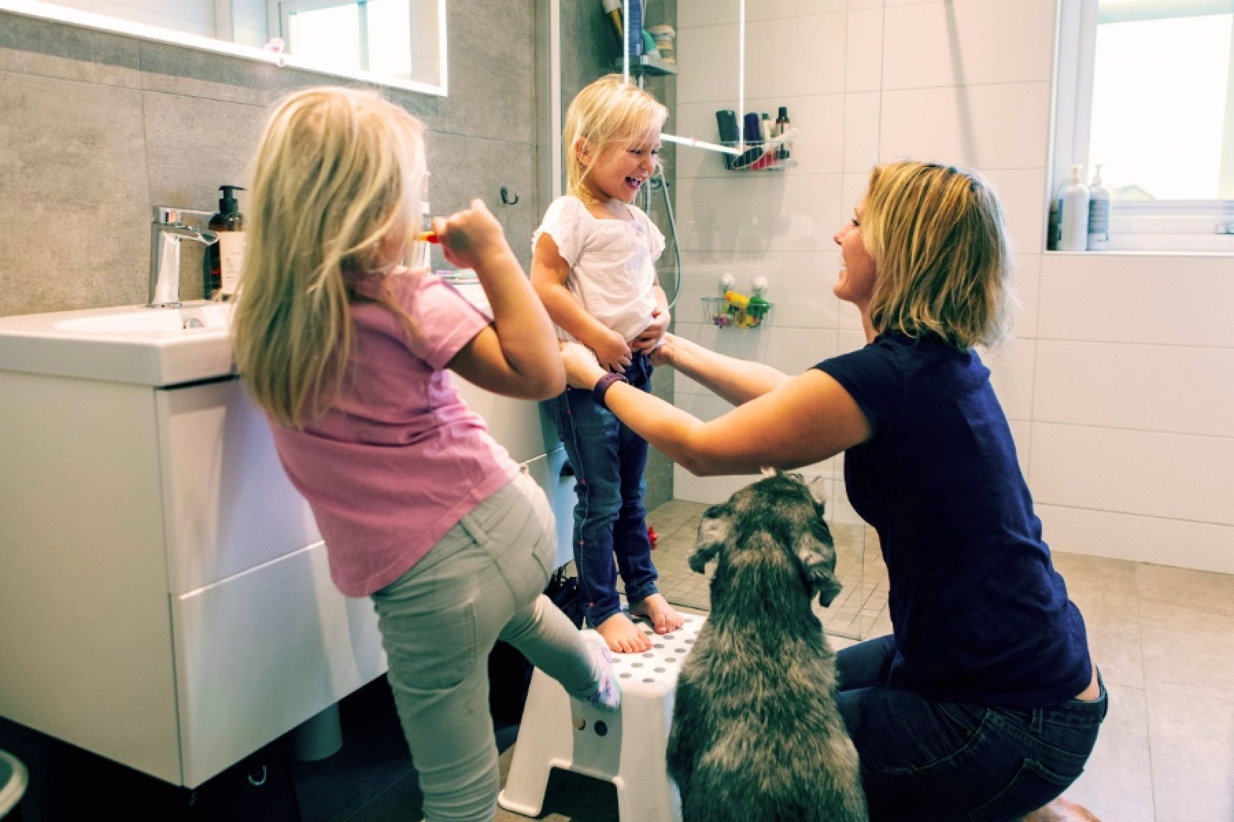 Eine junge Mutter mit zwei Kindern im Badezimmer beim Zähneputzen.