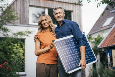 Ein Ehepaar steht vor seinem Haus mit einem Solarpanel in den Händen.
