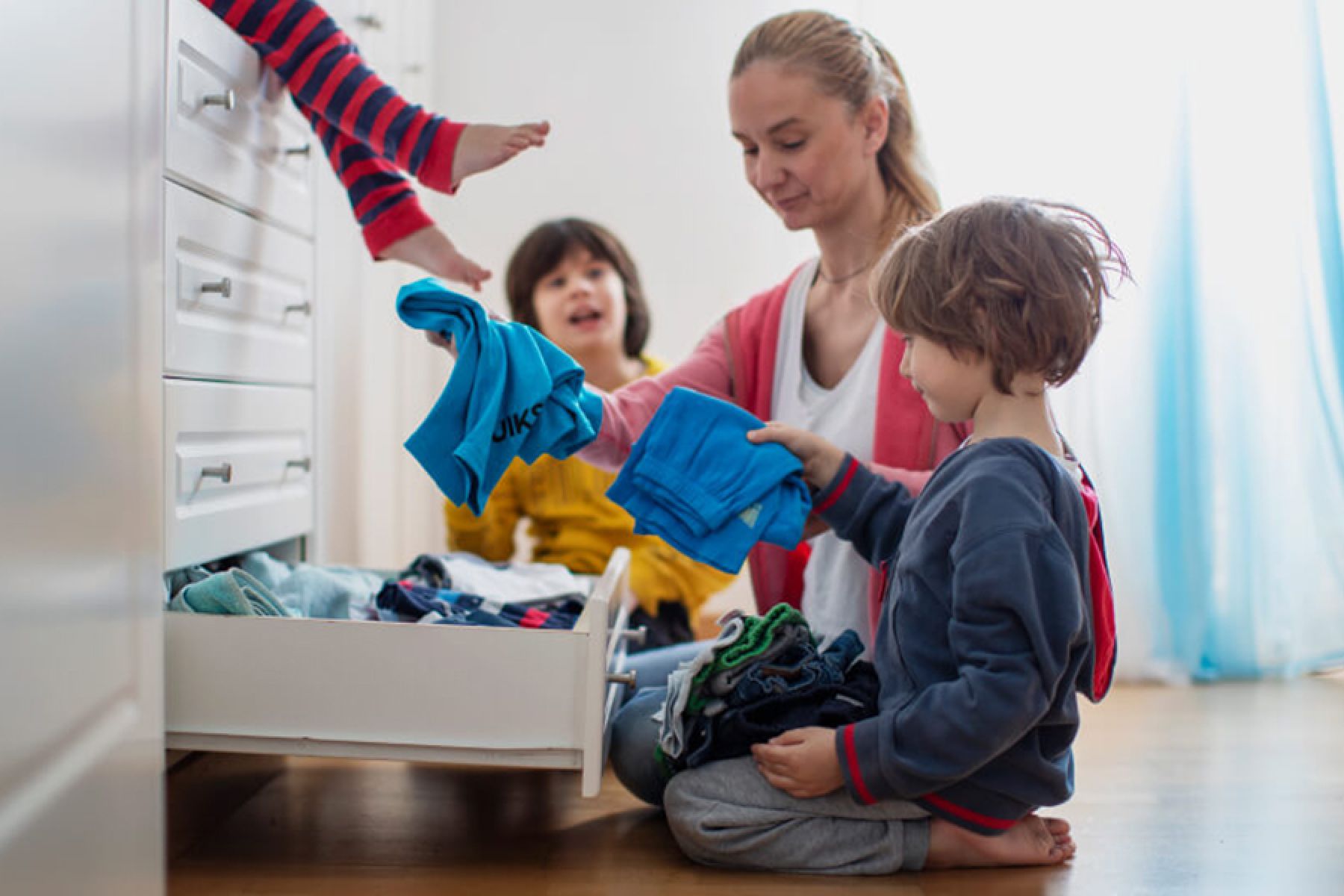 Eine Mutter räumt gemeinsam mit ihren Kindern eine Kleiderkommode auf.