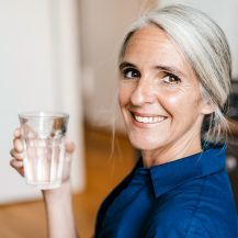 Eine lächelnde Frau, die ein Glas Wasser hält.