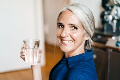 Eine lächelnde Frau, die ein Glas Wasser hält.