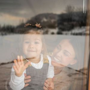 Eine Mutter schaut mit ihrer Tochter durch ein Wohnungsfenster. 