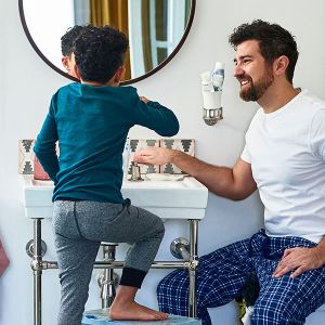 Vater und Sohn stehen gemeinsam im Badezimmer vor einem Waschbecken.