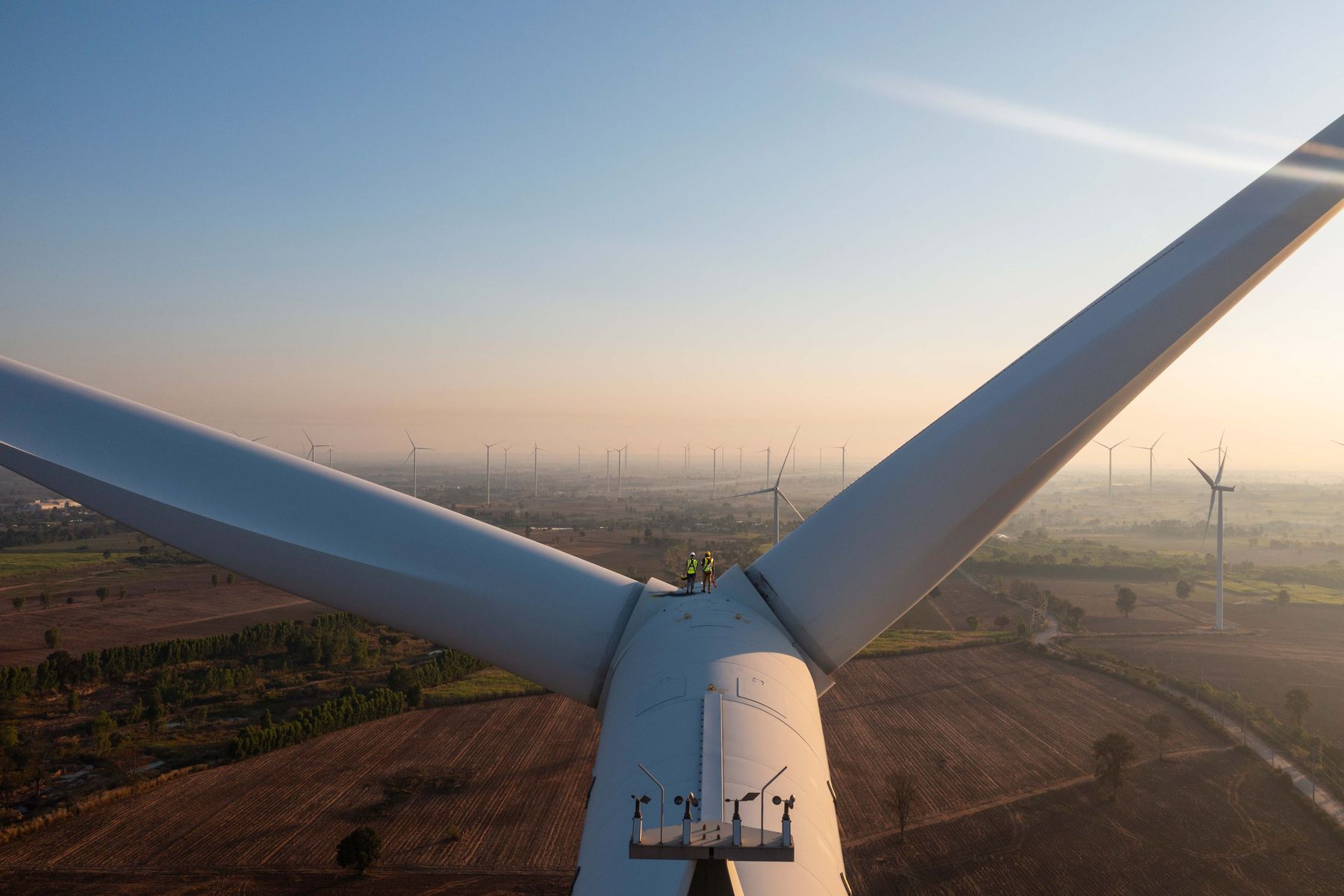 Zwei Monteure stehen zwischen den Rotorblättern einer Windkraftanlage.