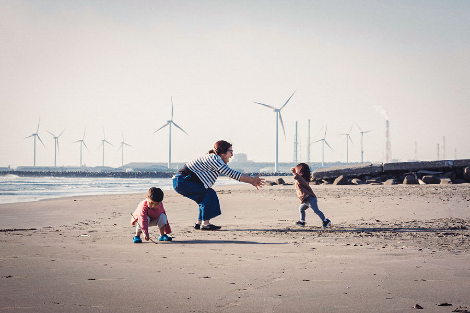 Eine junge Familie entspannt am Strand, im Hintergrund ist ein Windpark zu sehen.