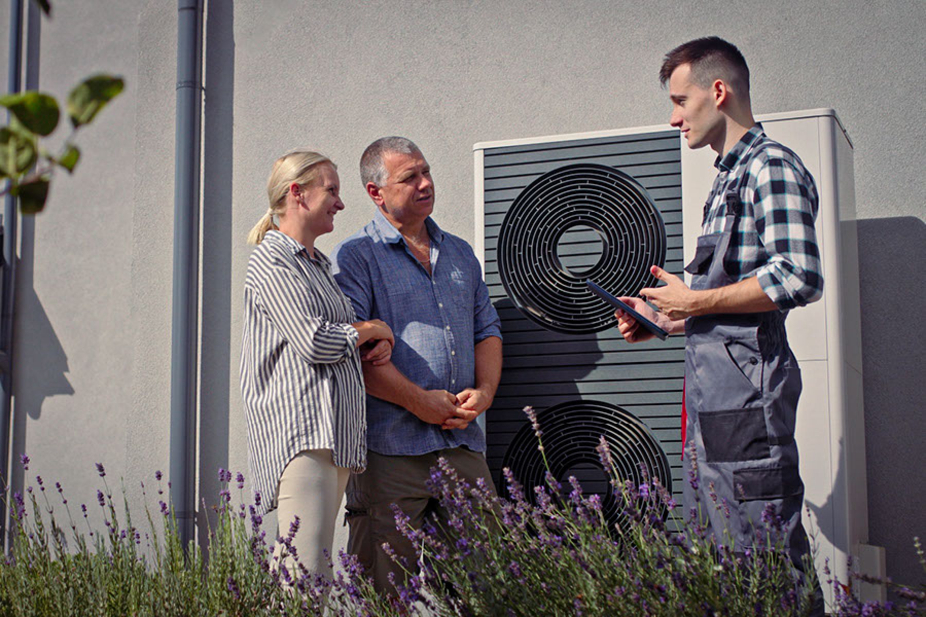 Ein Servicetechniker erklärt einem Ehepaar die Funktionen ihrer Wärme-pumpe. 