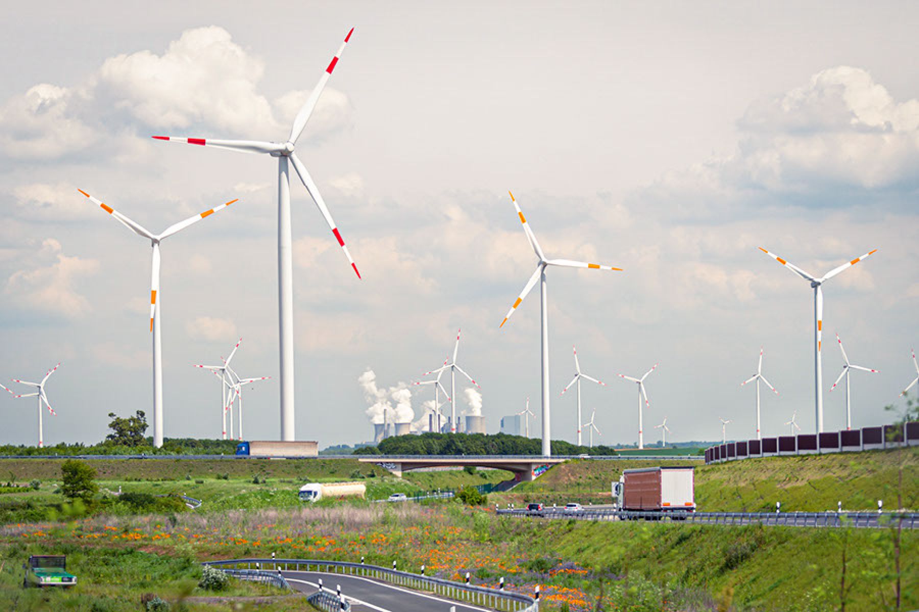 Ansicht einer Landschaft mit einer Landstraße im Vordergrund sowie einem Windpark und Industrieanlagen im Hintergrund.
