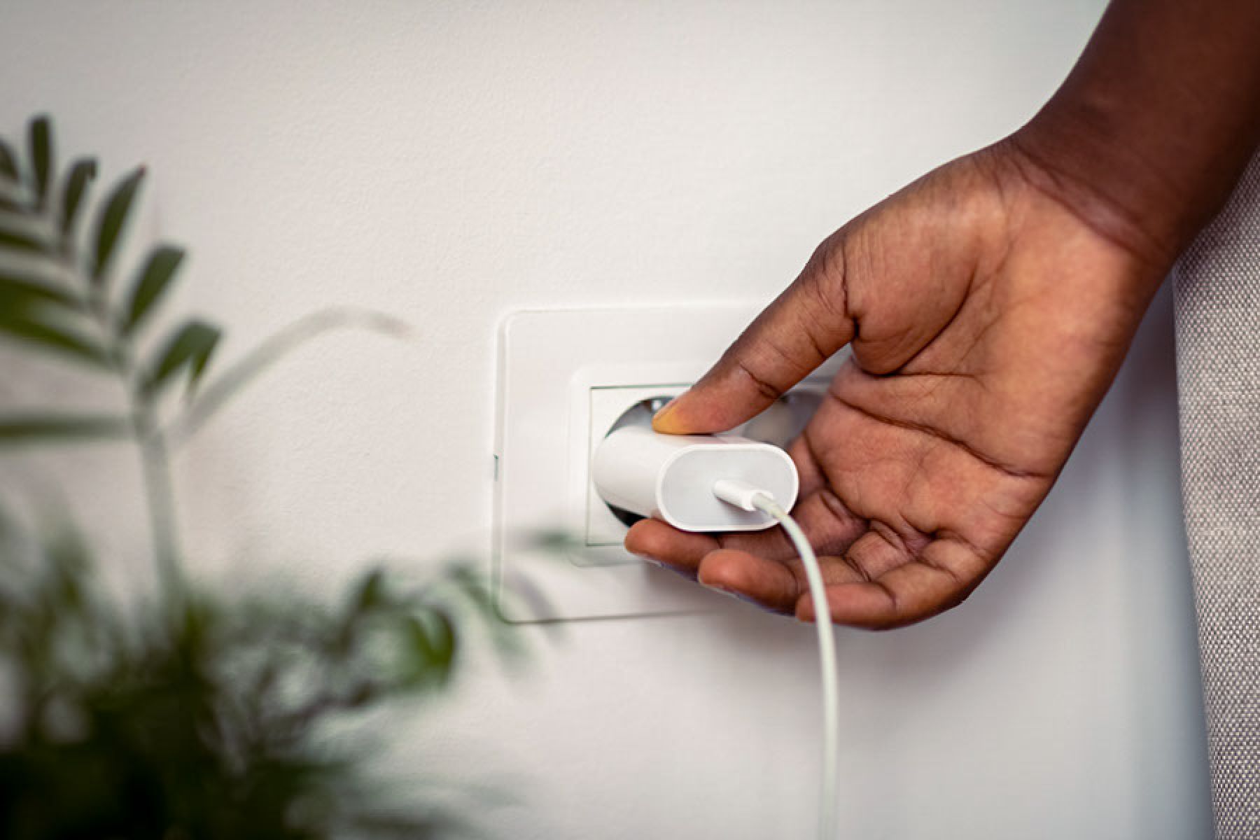Eine Hand hält den Adapter eines Ladeskabels, das in einer Steckdose steckt.