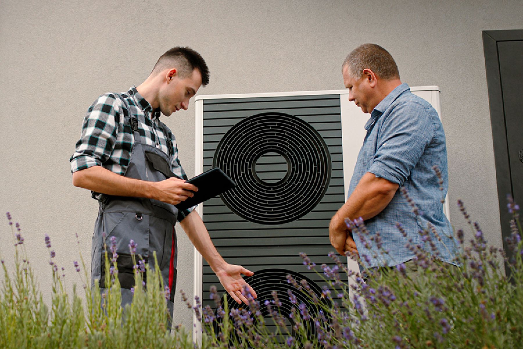 Ein Techniker berät sich mit einem Hausbesitzer über eine vor dem Haus installierte Wärmepumpe. 