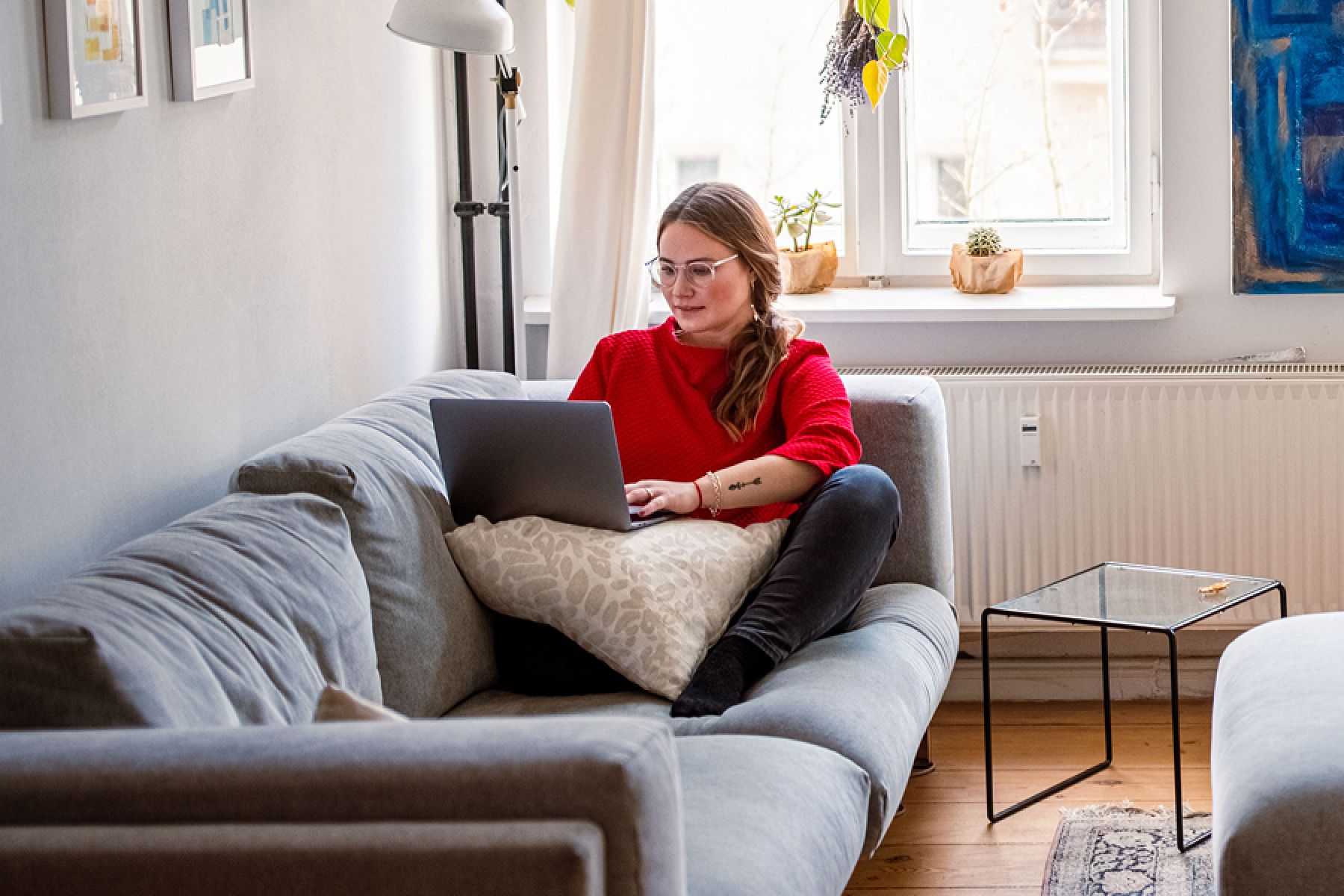 Eine junge Frau sitzt auf ihrem Sofa und nutzt ihren Laptop.