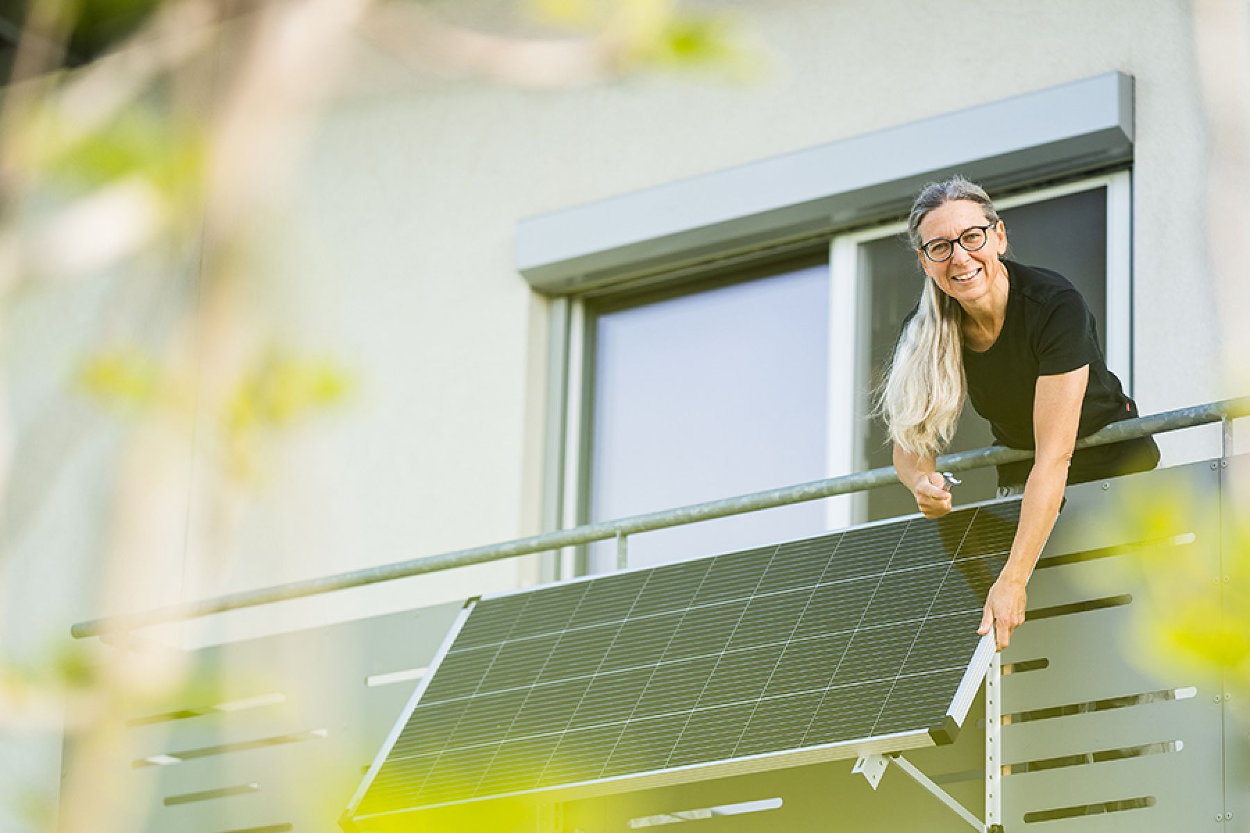 Eine lächelnde Frau installiert einen Sonnenkollektor an ihrem Hausbalkon.