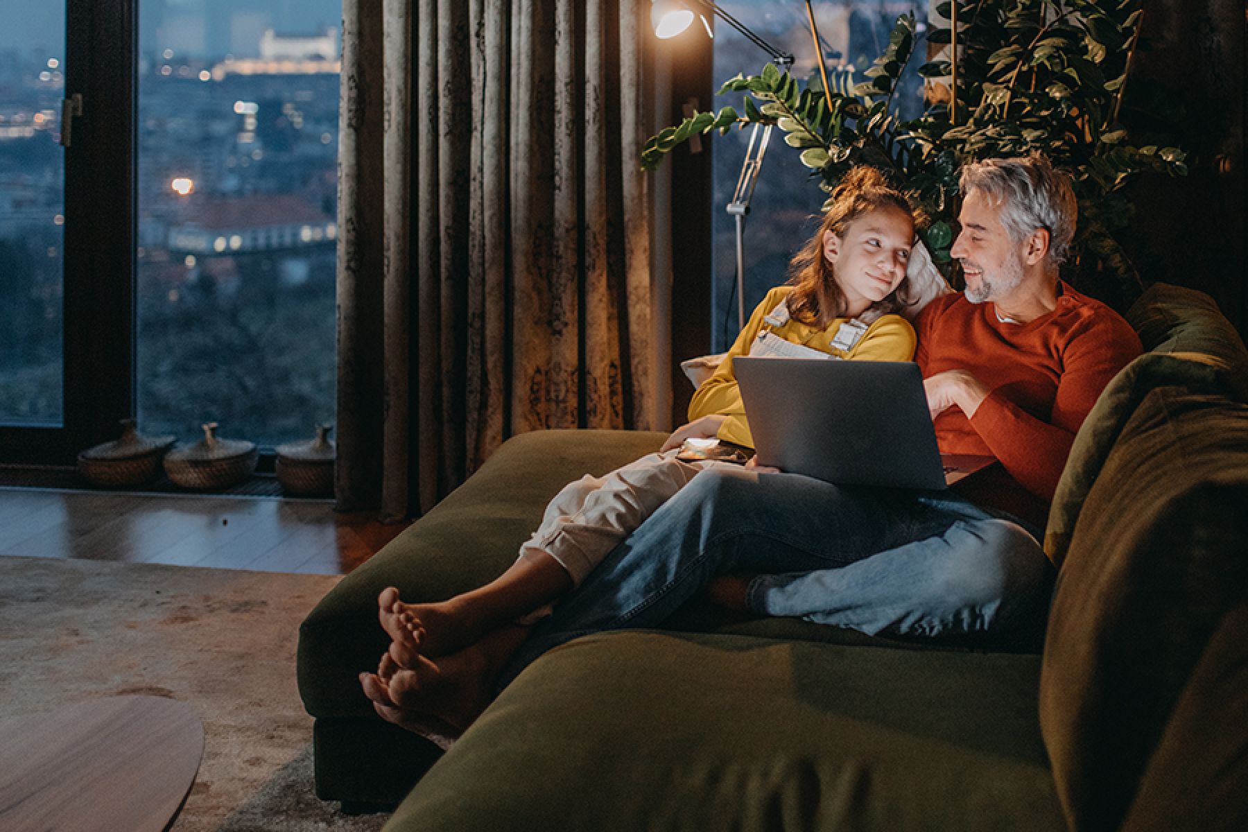 Vater und Tochter sitzen auf dem Sofa und schauen sich zusammen einen Film auf dem Laptop an. 