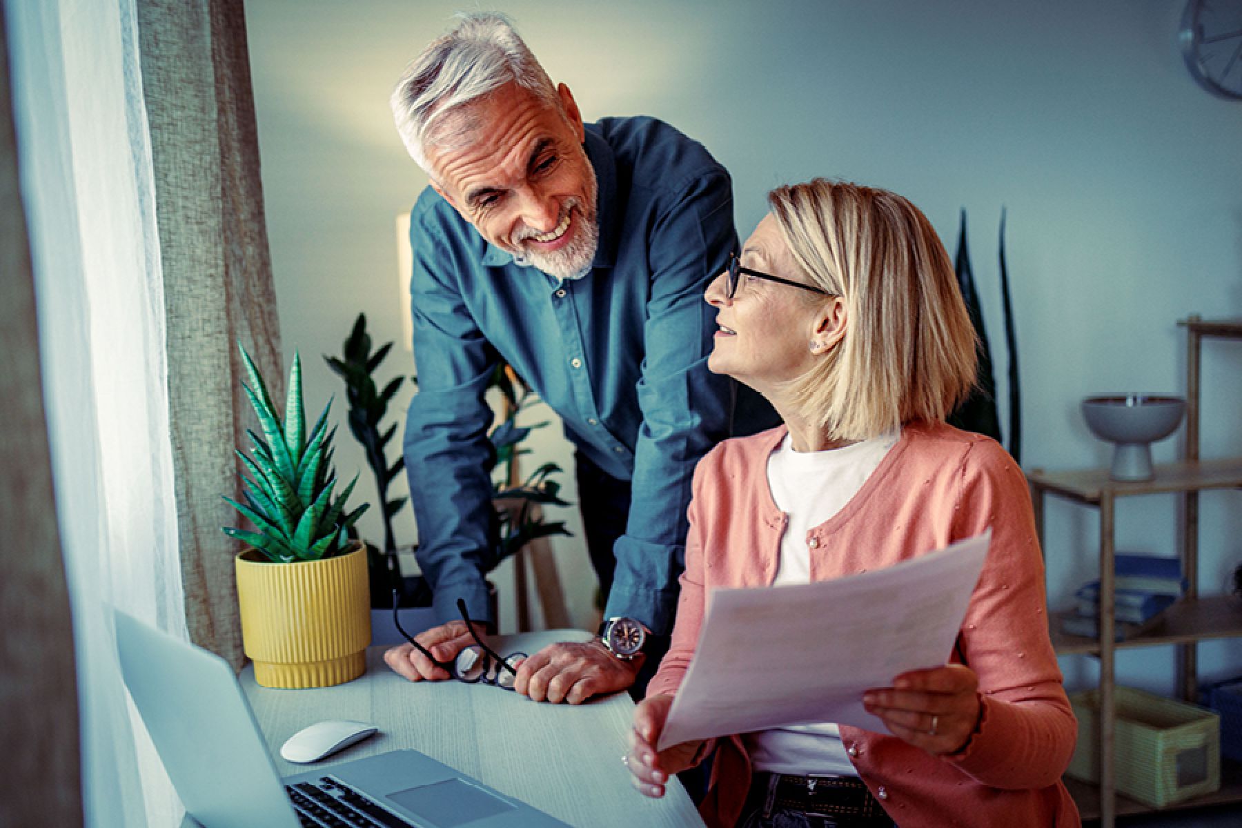 Lächelndes reifes Paar überprüft am Schreibtisch gemeinsam ein Dokument.