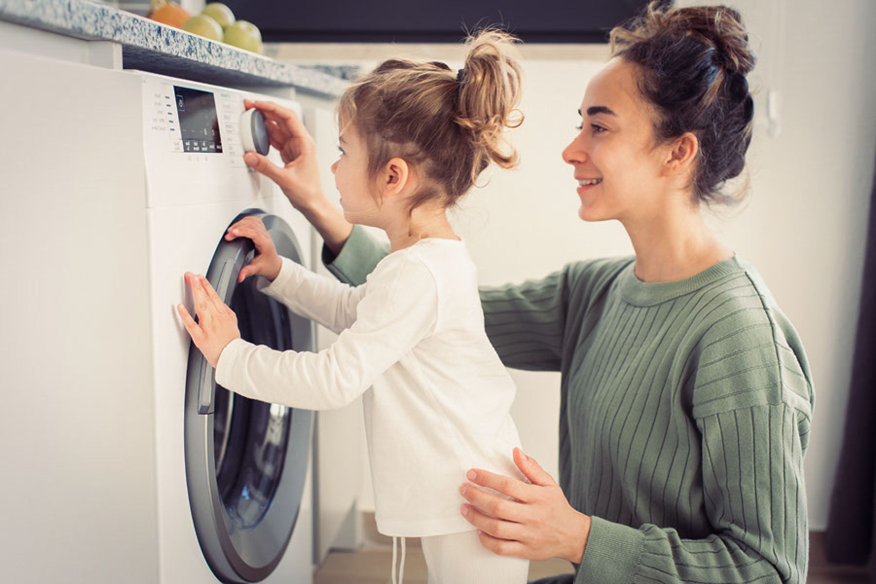 Eine Mutter mit ihrer kleinen Tochter vor einer Waschmaschine.    