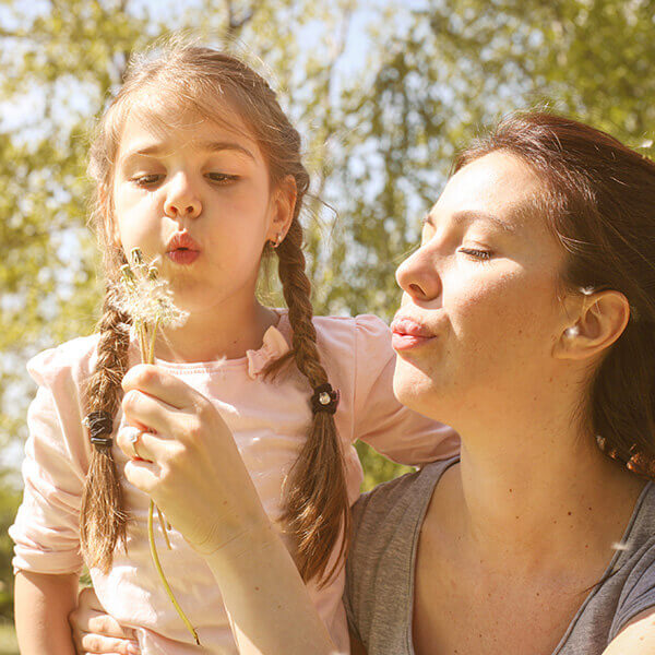 Mutter und Kind beim Ausblasen einer Pusteblume.