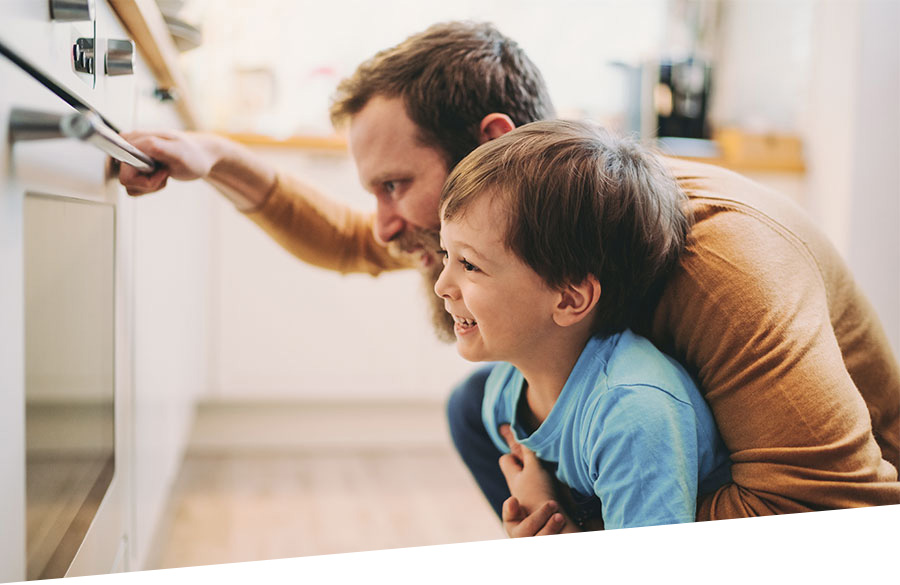 Energiesparend backen und kochen. Ein Vater beobachtet mit seinem Sohn das Garen der Speisen im Backofen.