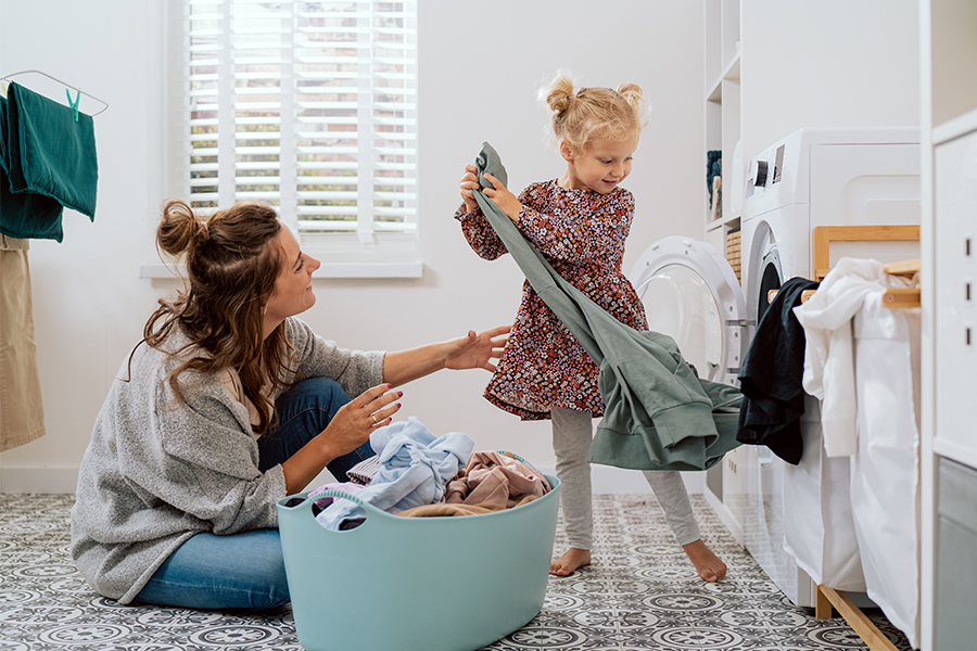 Mutter und Tochter holen im Badezimmer die frische Wäsche aus der Waschmaschine.