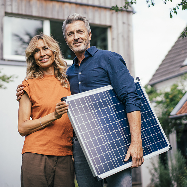 Ein Ehepaar steht vor seinem Haus mit einem Solarpanel in den Händen.