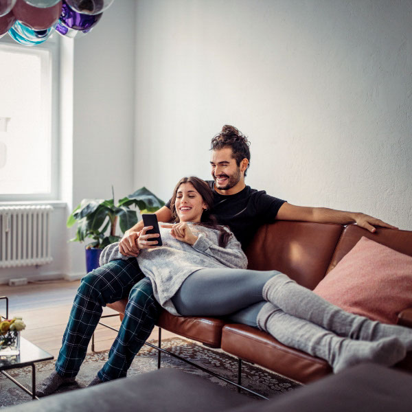 Ein junges Paar sitzt im Wohnzimmer auf dem Sofa. 