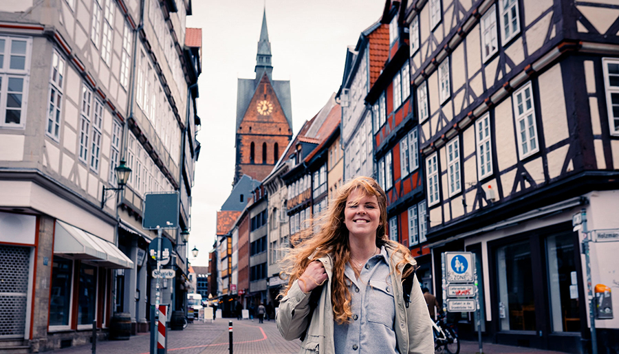 Eine junge Frau spaziert durch die Altstadt von Hannover, im Hintergrund sind Fachwerkhäuser zu sehen.