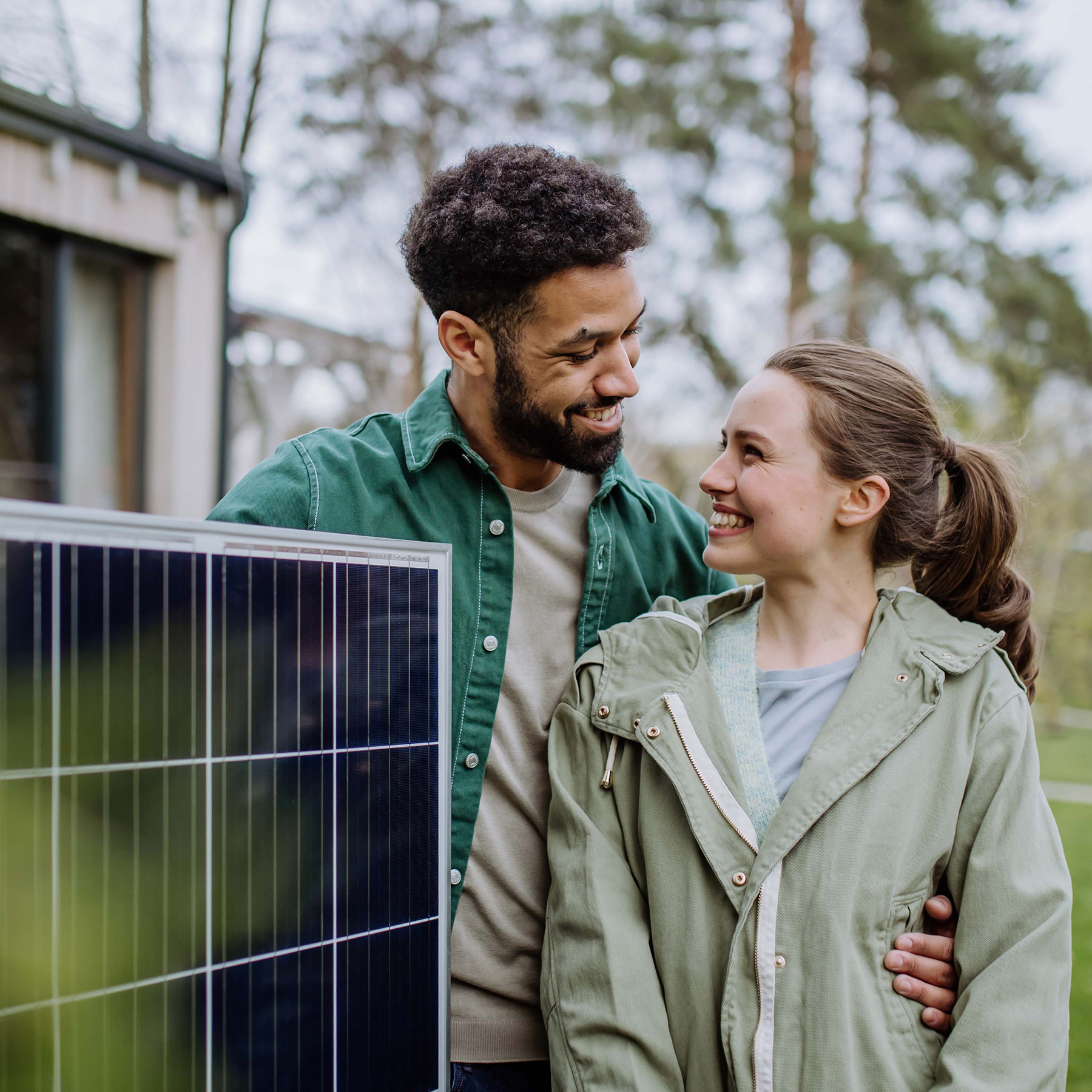 Ein junges Paar mit einem Solarmodul vor einem Haus.