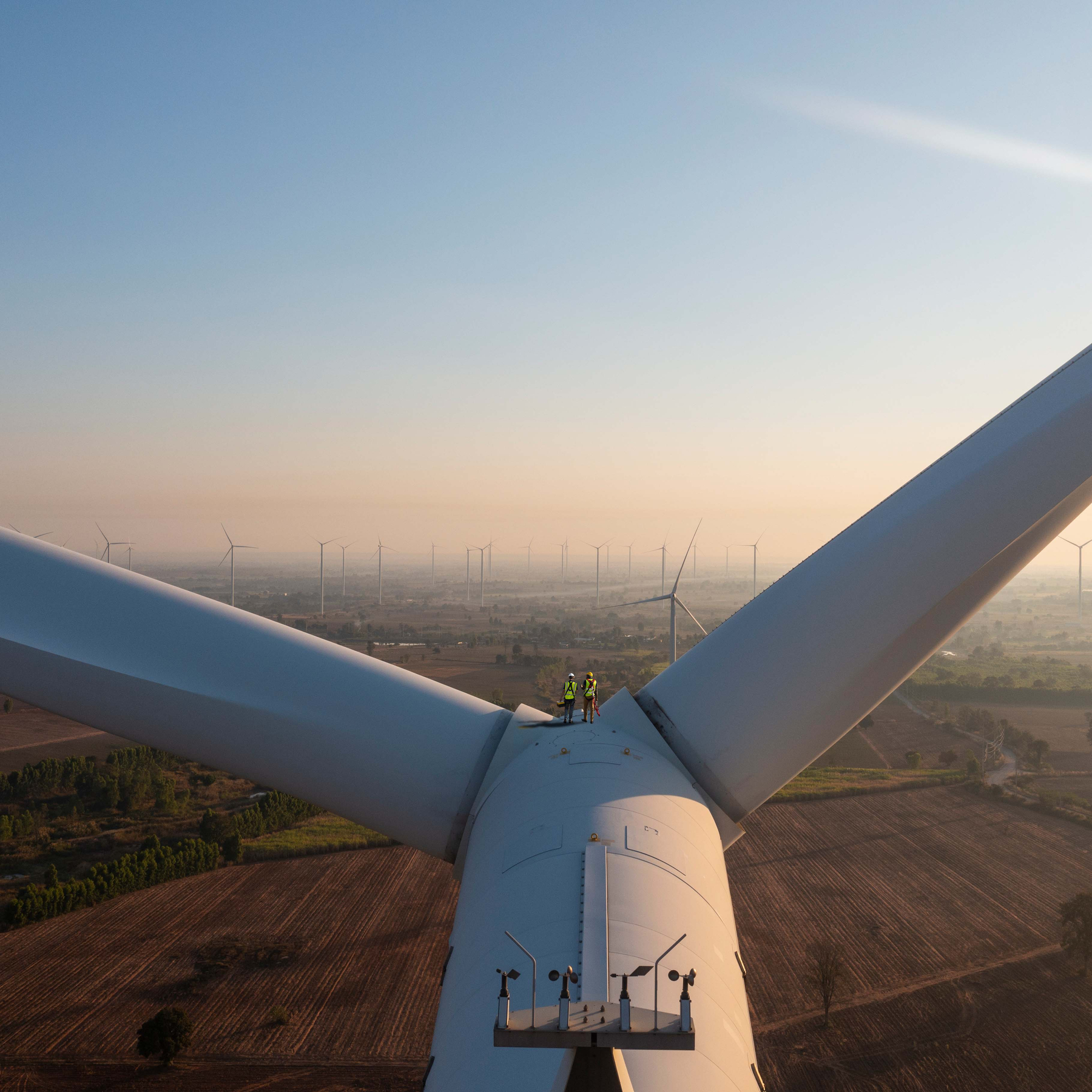 Zwei Monteure stehen zwischen den Rotorblättern einer Windkraftanlage.