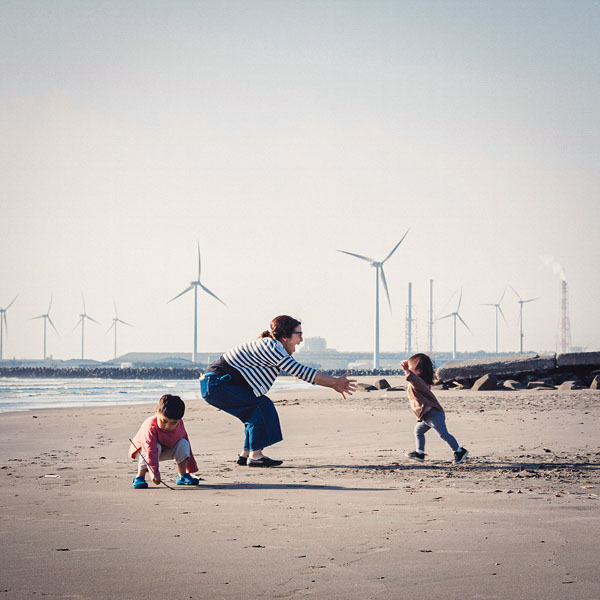 Eine junge Familie entspannt am Strand, im Hintergrund ist ein Windpark zu sehen.