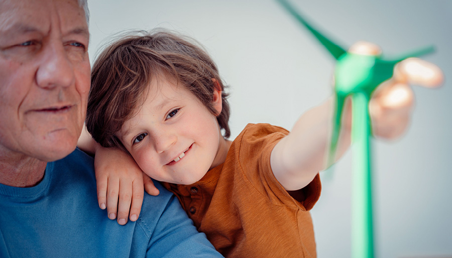 Lächelnder Junge, der mit seinem Großvater zu Hause das Modell einer Windenergieanlage betrachtet.