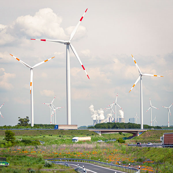 Ansicht einer Landschaft mit einer Landstraße im Vordergrund sowie einem Windpark und Industrieanlagen im Hintergrund.