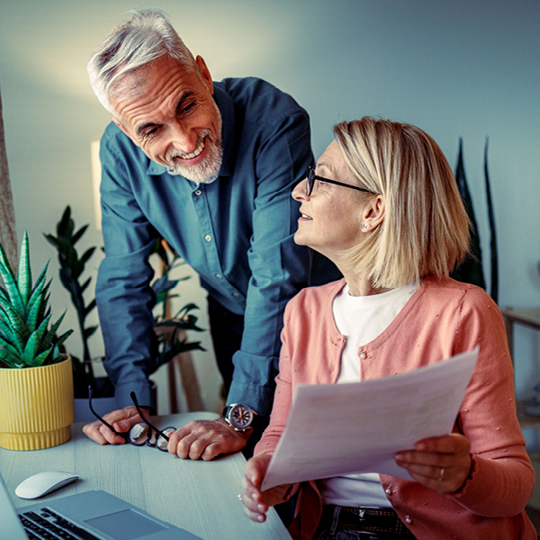 Lächelndes reifes Paar überprüft am Schreibtisch gemeinsam ein Dokument.